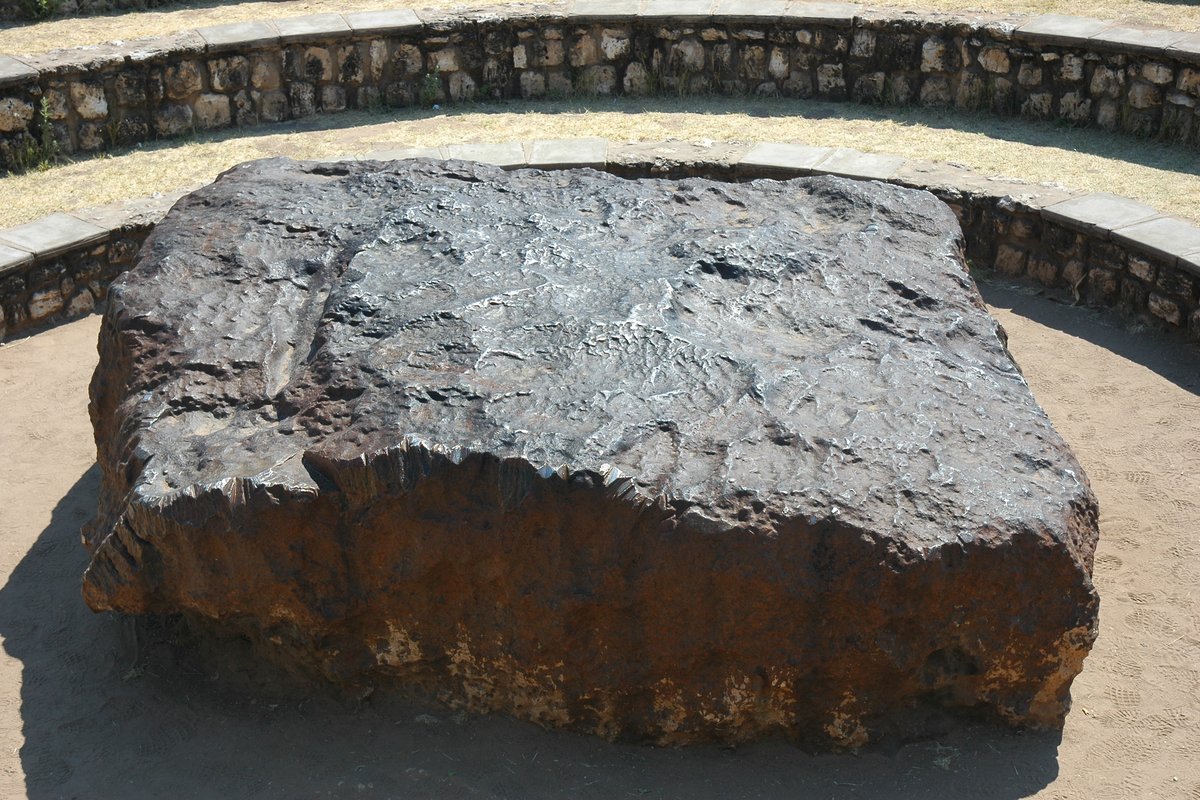 Photograph of The Hoba meteorite, a large flat-topped block of dark nickel-iron lying in its shallow excavated site near Grootfontein, Namibia.